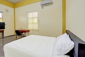 Ein Hotelzimmer mit Bett, Schreibtisch, Stuhl, Fernseher und Klimaanlage.