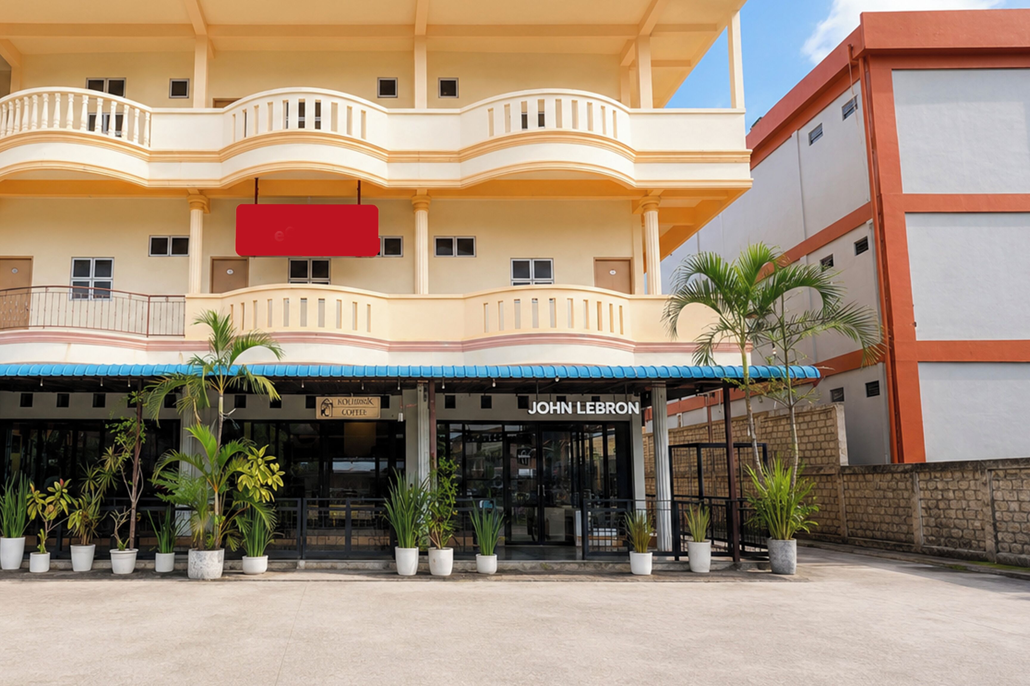 Un hotel con fachada de dos pisos, un balcón y una cafetería llamada 'John Lebron' en la entrada.