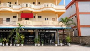 Un hotel con fachada de dos pisos, un balcón y una cafetería llamada 'John Lebron' en la entrada.