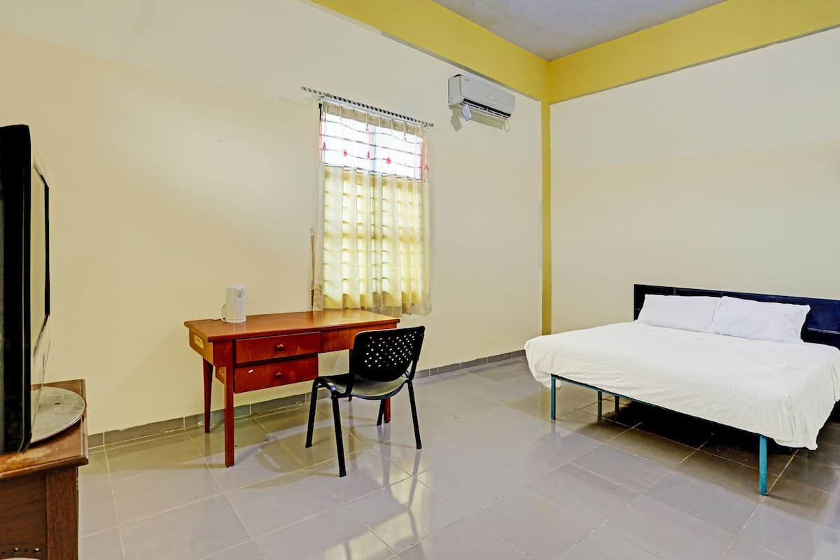 Quarto com uma cama, escrivaninha com cadeira, janela com cortinas e ar condicionado.