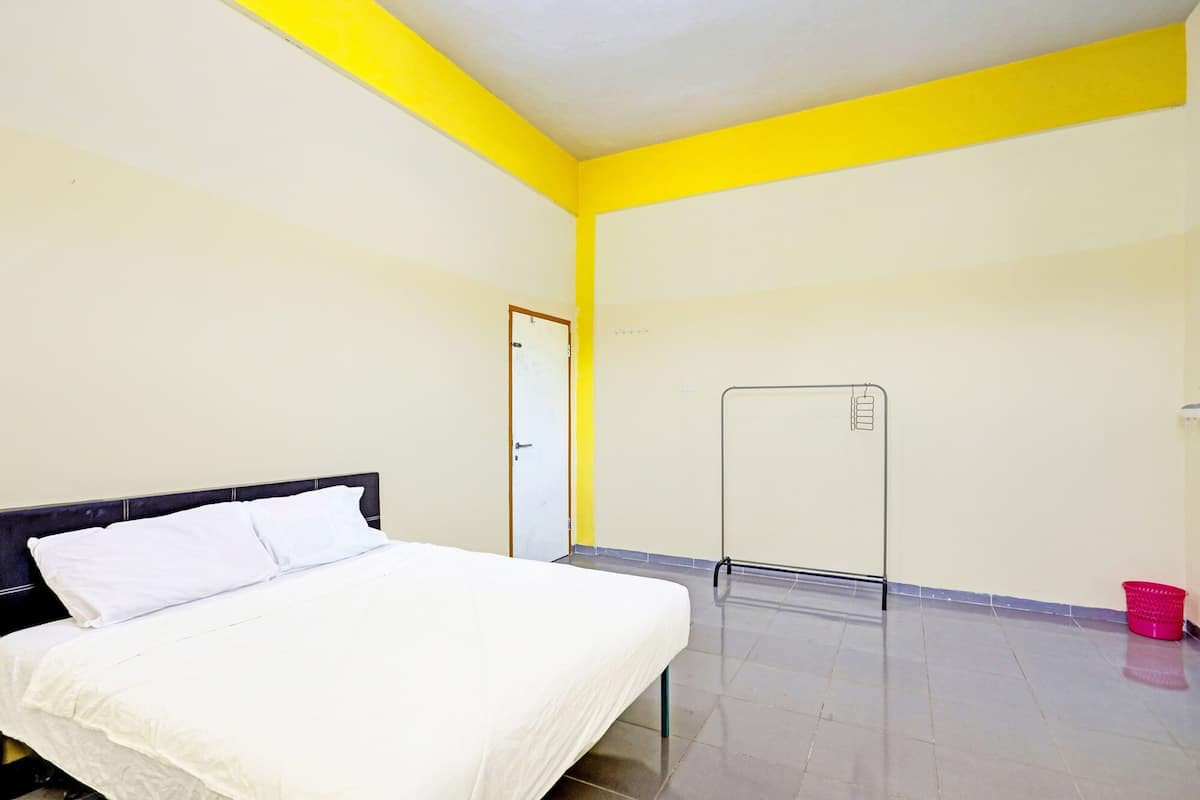 Quarto com uma cama, uma porta, um porta-toalhas e um balde vermelho.