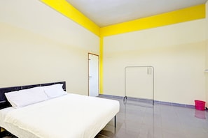 Una habitación con cama, una puerta, un perchero y un cubo rojo.