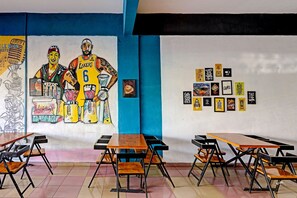 Una habitación con mesas y sillas, un mural y varios objetos enmarcados en la pared.