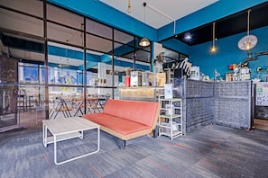 A modern office space with a sofa, tables, a coffee machine, and a brick-patterned counter.
