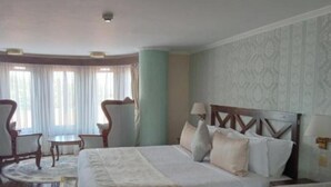 Une chambre d’hôtel avec un grand lit, deux chaises, une petite table et une fenêtre avec des rideaux.