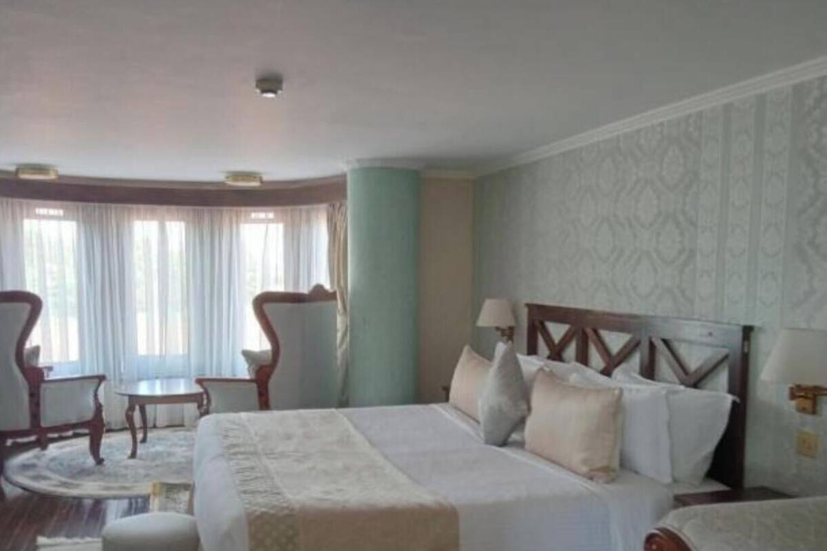 Una habitación de hotel con una cama grande, dos sillas, una mesita y una ventana con cortinas.