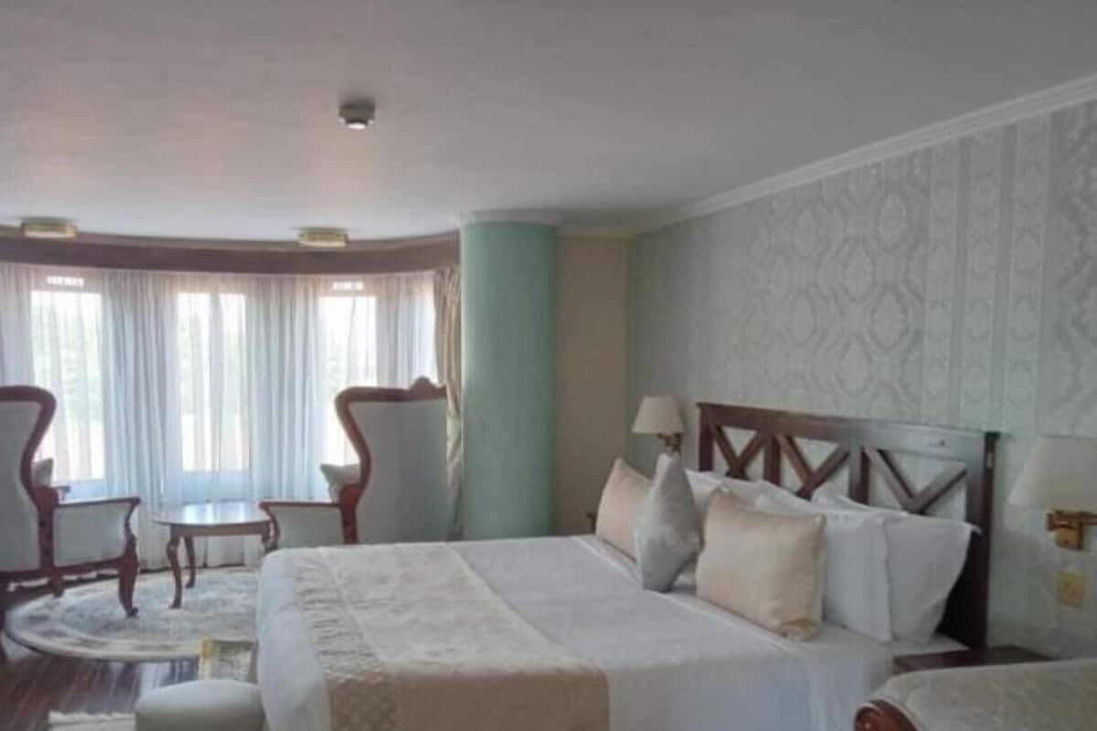 A hotel room with a large bed, two chairs, a small table, and a window with curtains.