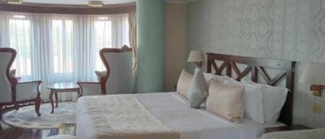 Una habitación de hotel con una cama grande, dos sillas, una mesita y una ventana con cortinas.