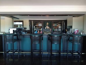 A bar area with a counter, bar stools, and a variety of bottles. - The Treetops Lodge (Aberdare National Park)