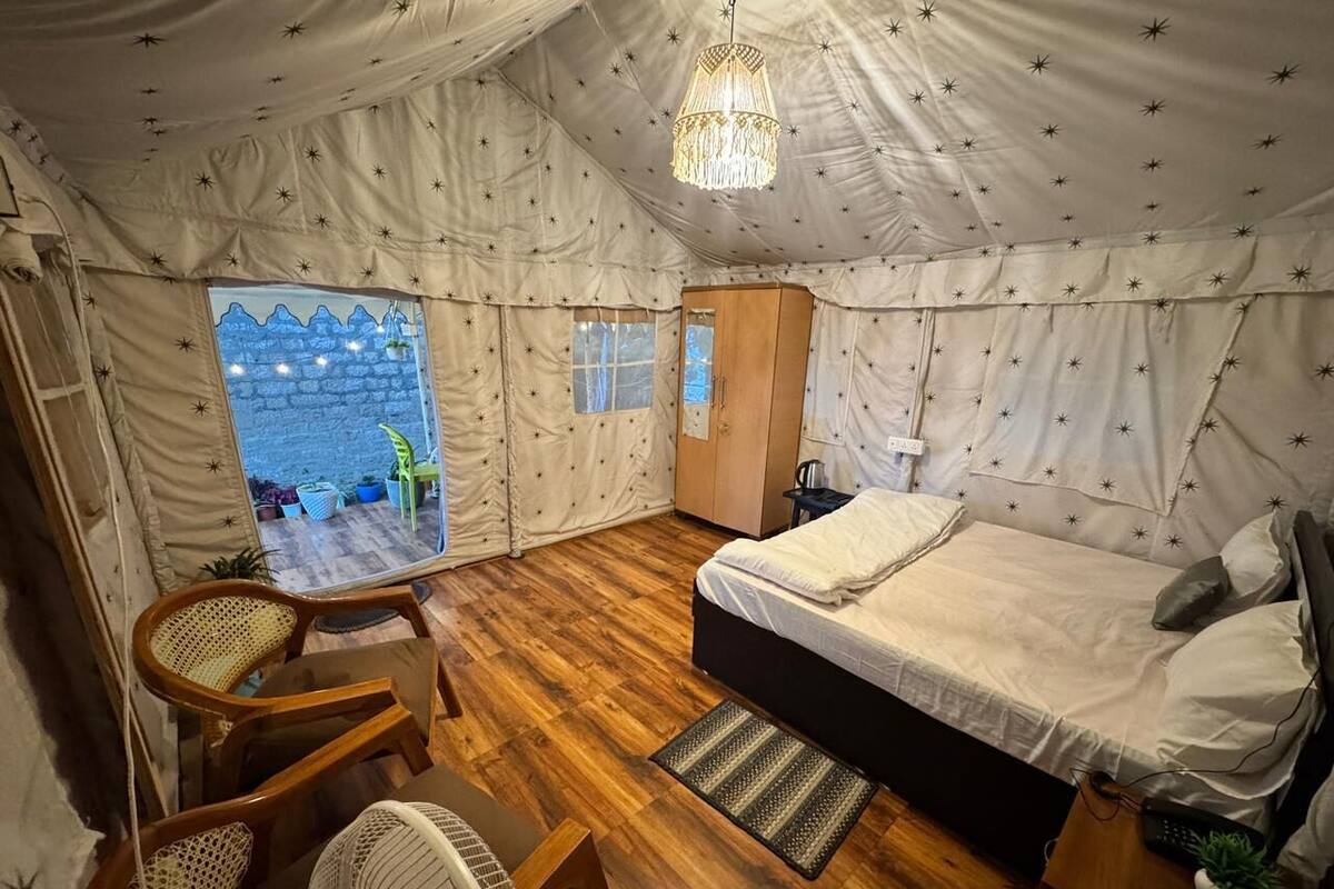 Una tienda de campaña con una cama, sillas de madera, una mesita y una lámpara colgante.