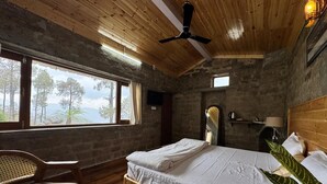A bedroom with a bed, a chair, a window with a view, and a ceiling fan.