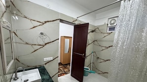 A bathroom with a marble wall, a sink, a shower curtain, and a door leading to another room.