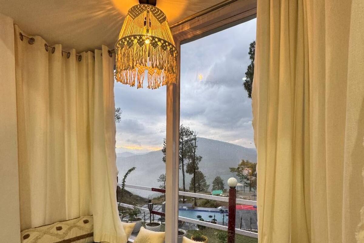 Una habitación con cama frente a una ventana, cortinas, una lámpara colgante y vista a un paisaje montañoso.