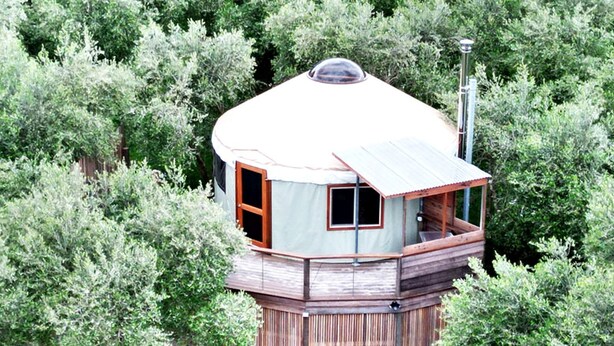 Una casa torre de madera con balcón, rodeada de abundante vegetación.