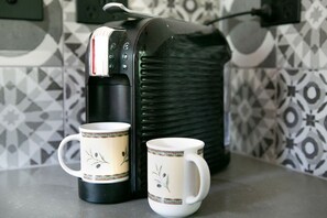 Une cuisine équipée d’une machine à café, de deux tasses et d’un crédence décorée.