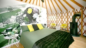 Una habitación tipo tienda de campaña con una cama, un mural en la pared, una mesita con una silla y un estufa de leña.