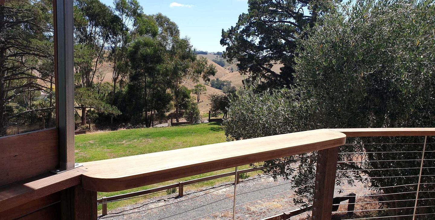 A wooden deck with a metal railing overlooking a grassy area with trees and hills.