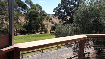 A wooden deck with a metal railing overlooking a grassy area with trees and hills.