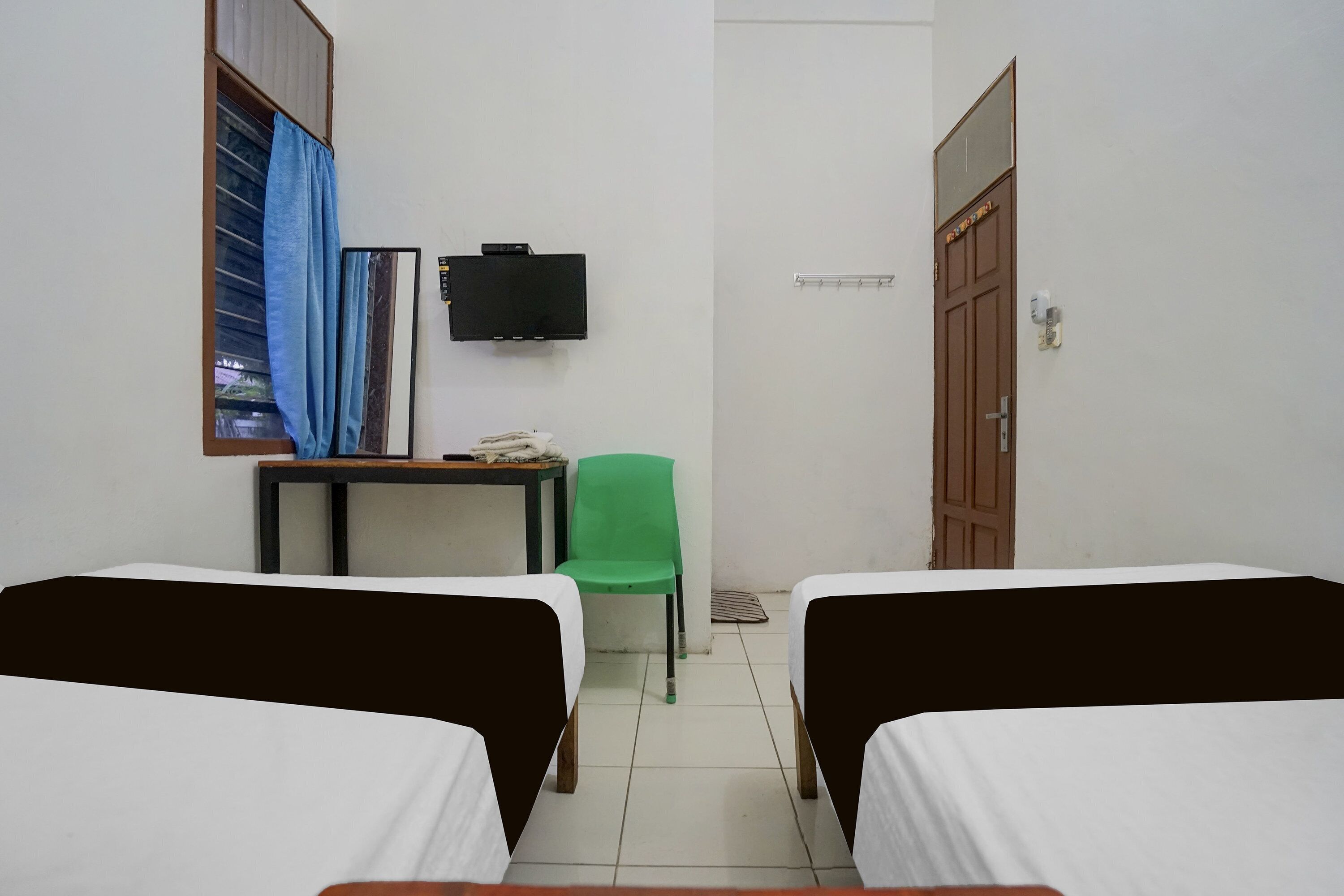 Una habitación con dos camas, una mesa con una silla, un televisor y una puerta.
