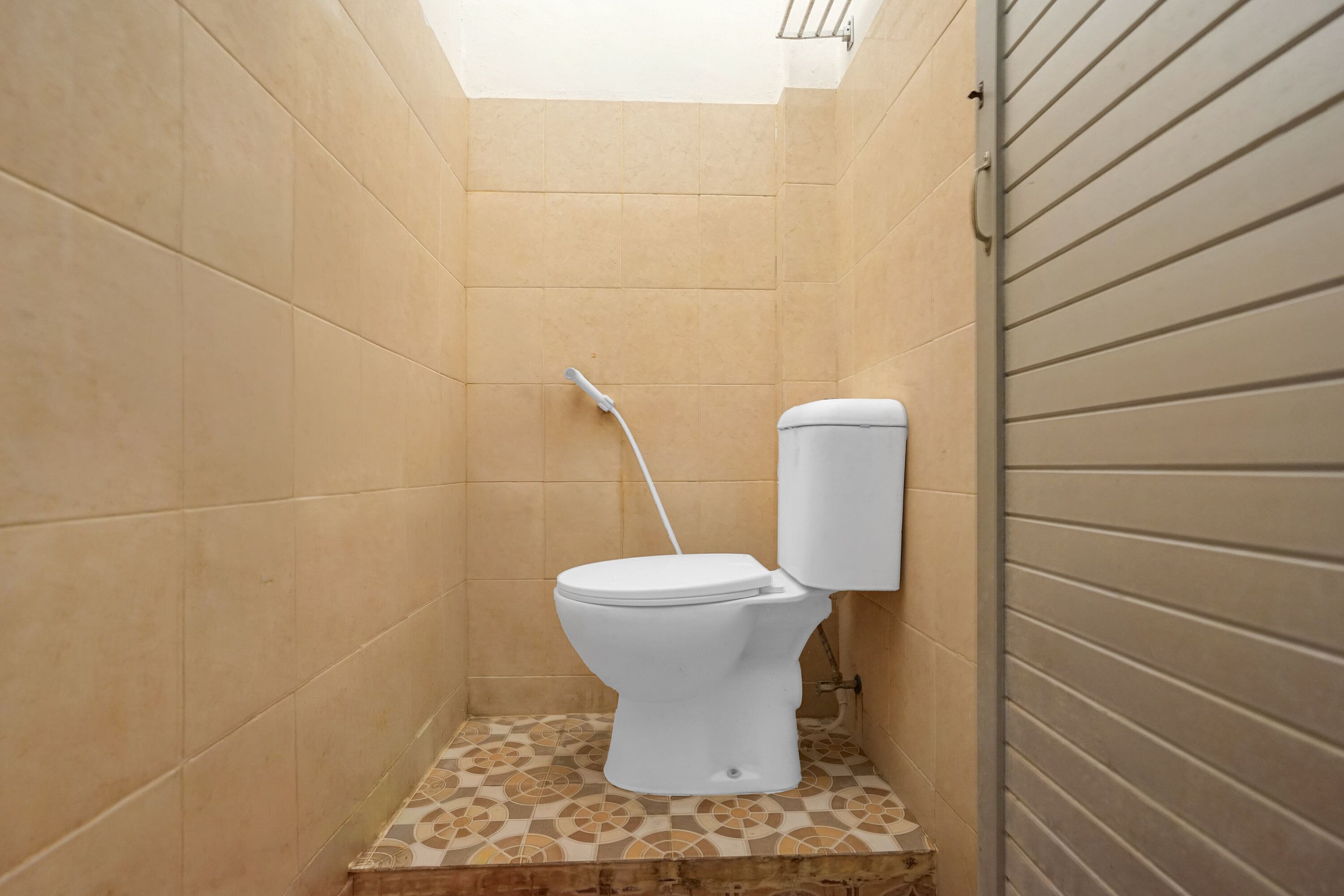 A small, enclosed bathroom with a toilet, a shower head, and a tiled floor.