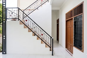 Una escalera con barandilla de metal y detalles en rojo, que conduce a una puerta con ventanal.
