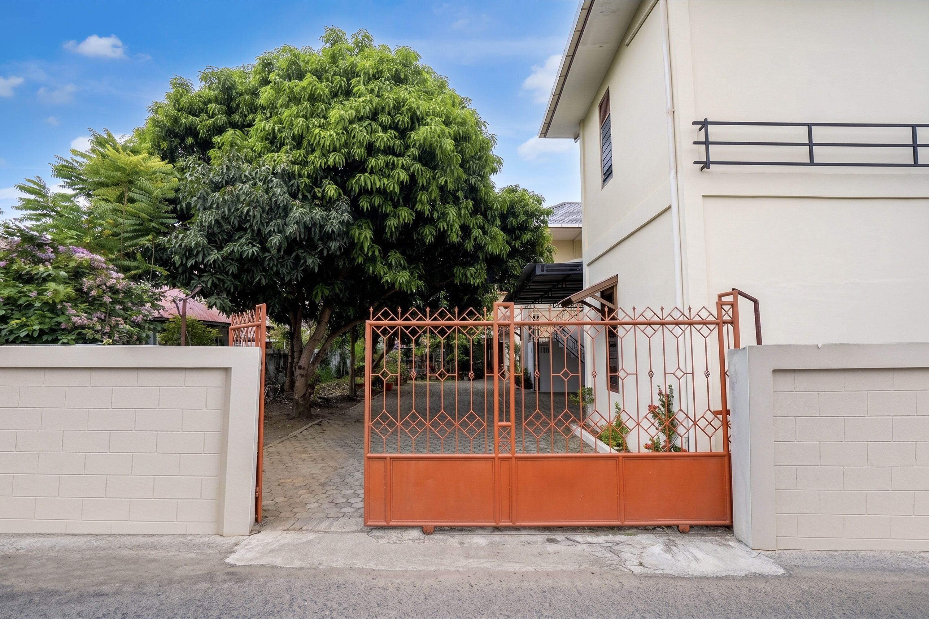 Una entrada con portón a un edificio, con un camino pavimentado y un árbol grande al fondo.