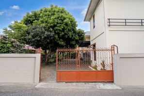 Uma entrada gradeada para um edifício, com um caminho de paralelepípedos e uma grande árvore ao fundo.