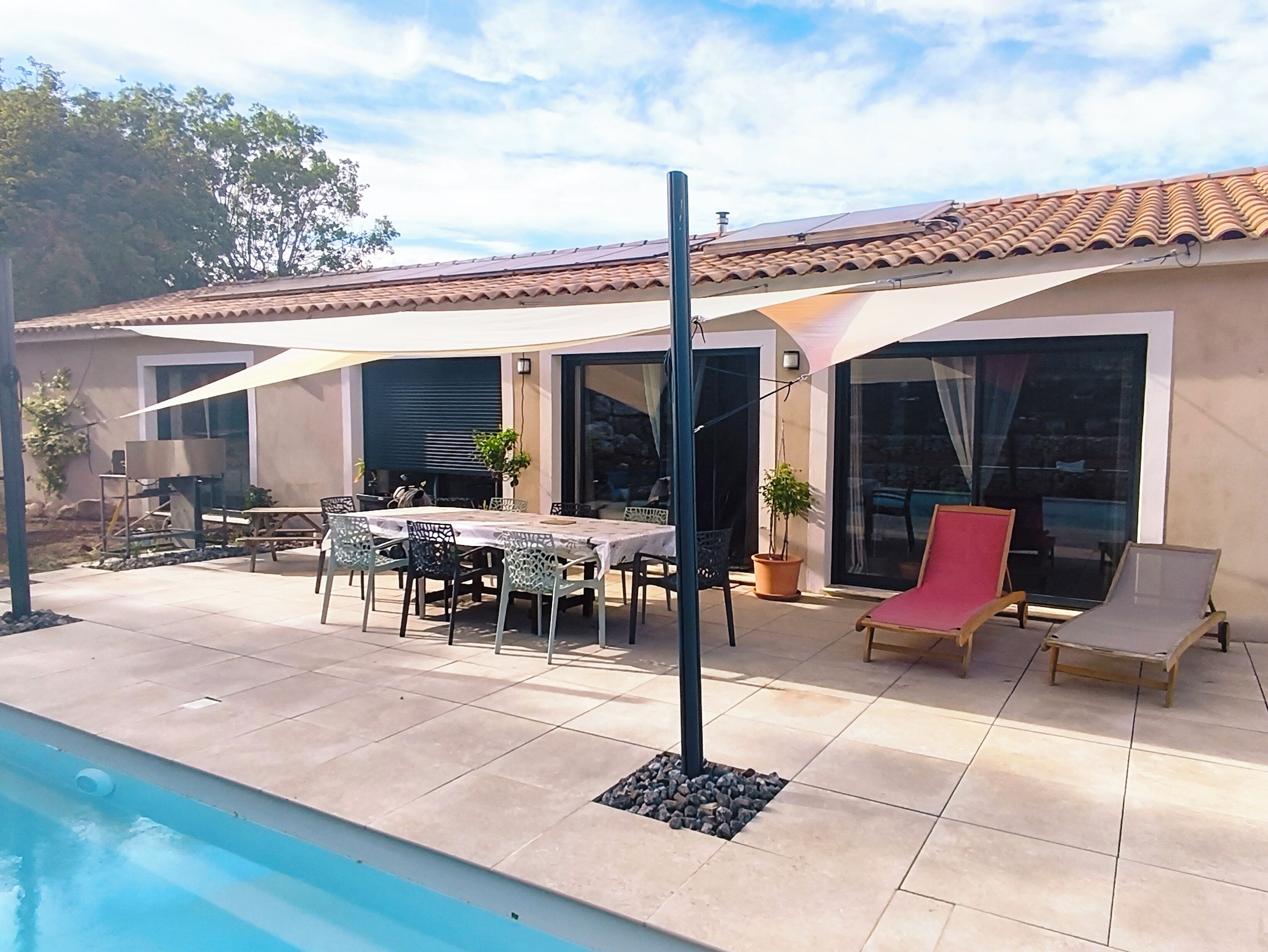 A poolside area with a table and chairs, a lounge chair, and a pergola.
