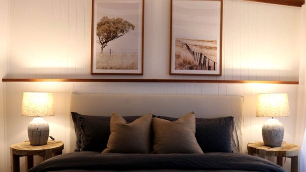 Een slaapkamer met een bed, twee nachtkastjes, twee lampen en twee foto’s in lijsten aan de muur.