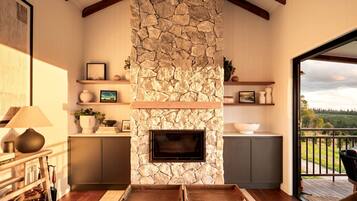 A living room with a stone fireplace, wooden beams, a sofa, and a view of the outdoors.