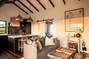 A modern interior with a kitchen, dining area, and living room, featuring wooden beams, pendant lighting, and a fireplace.