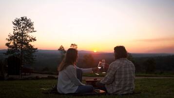 Two people sitting on a blanket outdoors during sunset, with a view of the landscape.