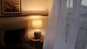 Un dormitorio con una cama, una lámpara de noche, un cuadro enmarcado en la pared y una ventana con cortinas.