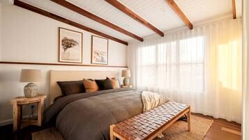 A bedroom with a large bed, wooden headboard, two bedside lamps, a bench, and framed artwork on the wall.