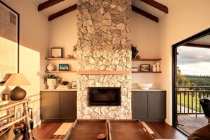 Una sala de estar con chimenea de piedra, vigas de madera, un sofá y vistas al exterior.