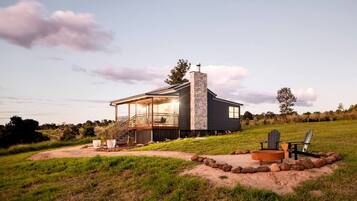 Uma casa moderna com chaminé de pedra, varanda coberta e um espaço para fogueira no quintal.