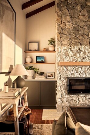 A cozy living room with a stone fireplace, wooden shelves, and a flat-screen TV.