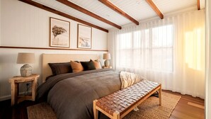 A bedroom with a large bed, wooden headboard, two bedside lamps, a bench, and framed artwork on the wall. - Stunning Cabin with a Private Hot Tub and Views of Bunya Mountain, Perfect for a Queensland Getaway (Neumgna)