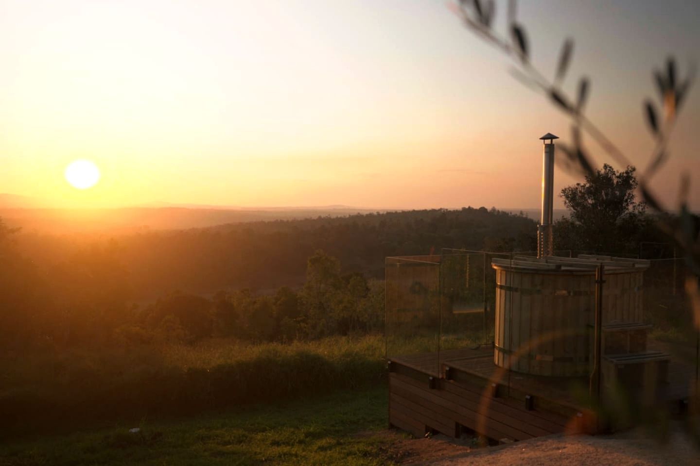 Una terraza de madera con una chimenea, con vistas a un paisaje boscoso durante el atardecer.