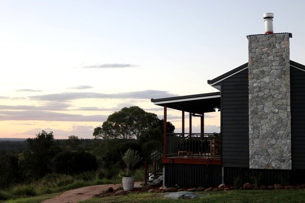 A modern house with a stone chimney, a covered porch, and a view of the surrounding landscape.