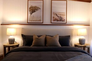 A bedroom with a bed, two nightstands, two lamps, and two framed pictures on the wall.