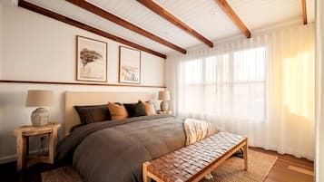 Une chambre à coucher avec un grand lit, une tête de lit en bois, deux lampes de chevet, un banc et des œuvres d’art encadrées accrochées au mur.