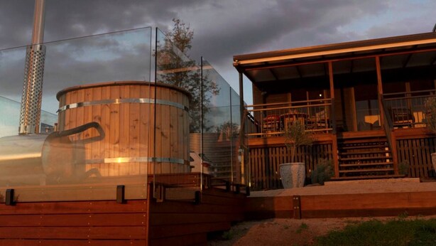 A wooden building with a large cylindrical tank, a covered outdoor seating area, and a staircase leading to a deck. - Stunning Cabin with a Private Hot Tub and Views of Bunya Mountain, Perfect for a Queensland Getaway (Neumgna)