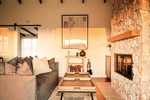 A cozy living room with a stone fireplace, a sofa with cushions, a coffee table, and a framed artwork above the fireplace.