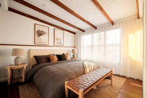 A bedroom with a large bed, wooden headboard, two bedside lamps, a bench, and framed artwork on the wall. - Stunning Cabin with a Private Hot Tub and Views of Bunya Mountain, Perfect for a Queensland Getaway (Neumgna)