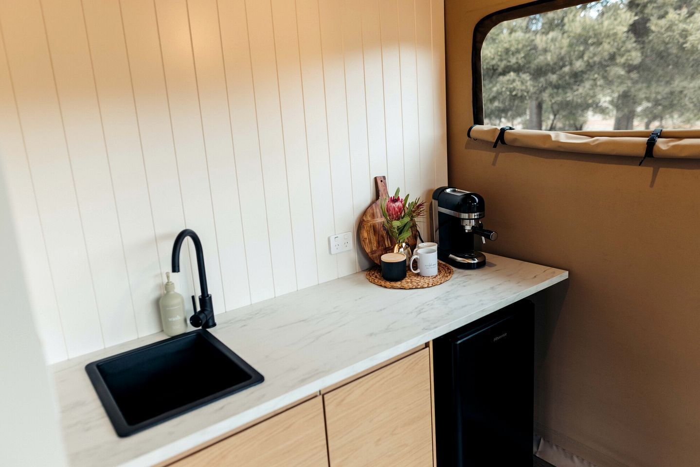 A compact kitchen with a black sink, a coffee maker, and a window with a view of trees.