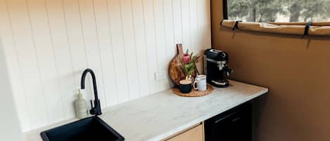 A compact kitchen with a black sink, a coffee maker, and a window with a view of trees.