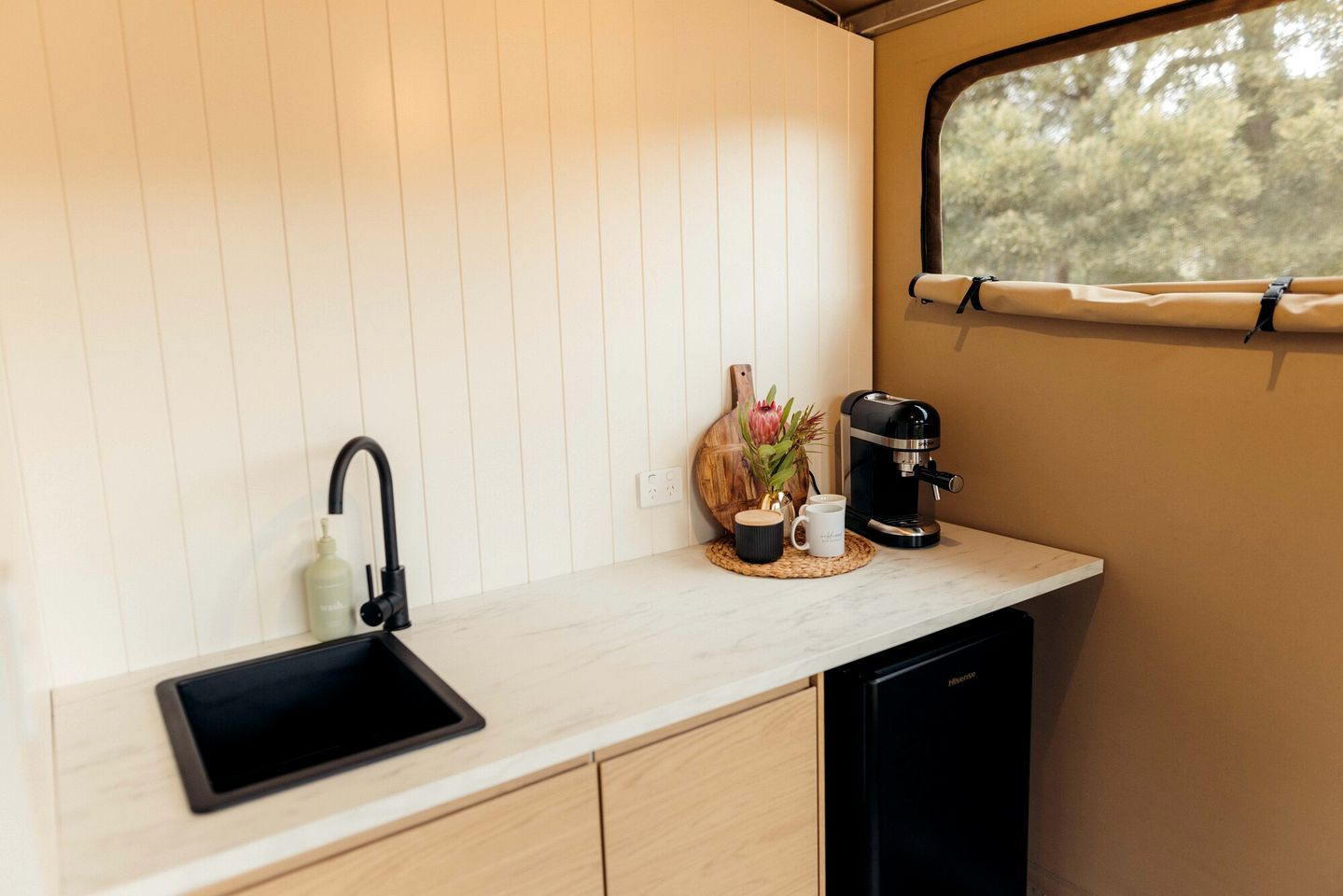 A compact kitchen with a black sink, a coffee maker, and a window with a view of trees.