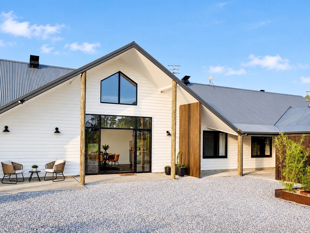 Une maison moderne avec un toit en pente, une grande porte d’entrée en verre et une allée gravillonnée.