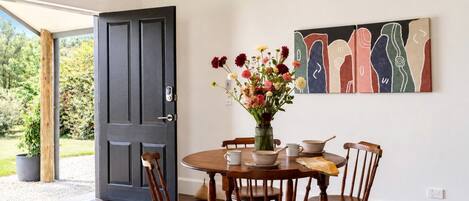 Un coin repas avec une table ronde en bois, six chaises, un vase de fleurs et un tableau accroché au mur.